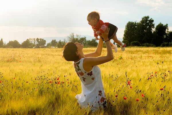 woman holding her daughter up to the sky while standing in a field of wheat