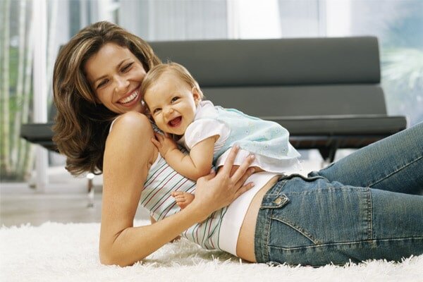 smiling woman laying on the floor with a baby on top of her