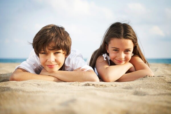 two children smiling and laying on the sand