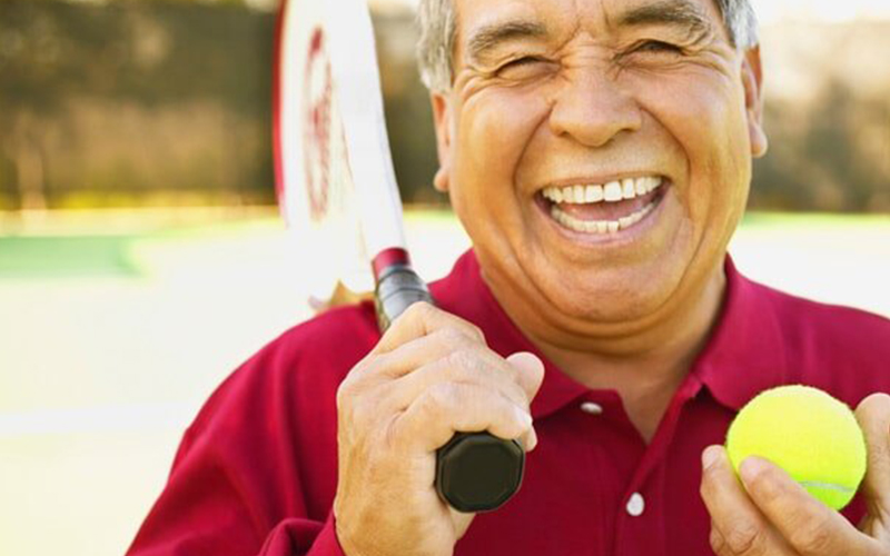 smiling older man with a tennis racket and ball in hand