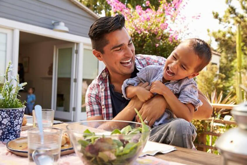 father playing with son outside while seated at a table