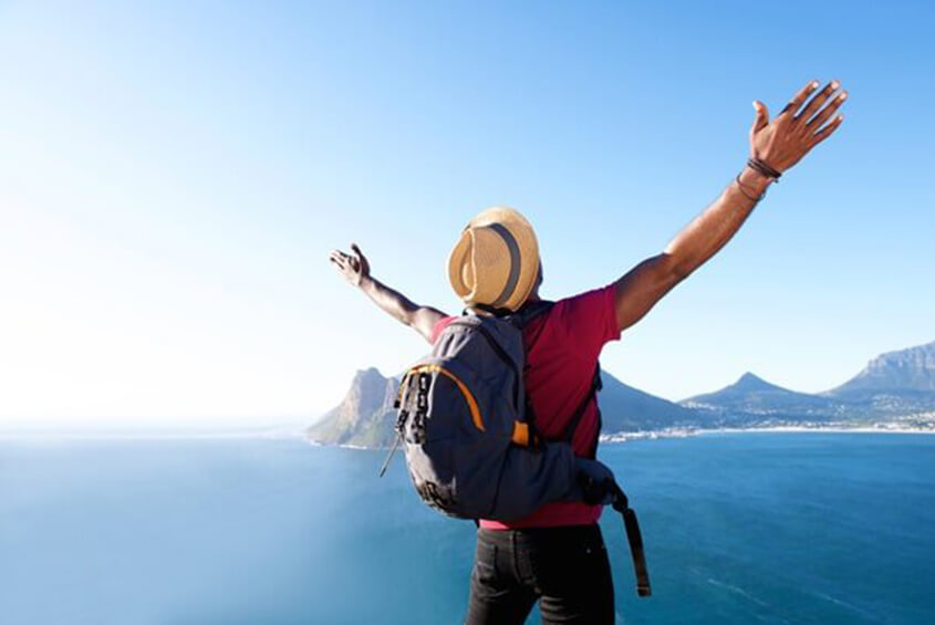 man wearing a blue backpack and hat spreading his arms while looking at an island